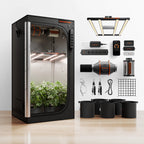 Black indoor grow tent with leafy plants, LED lights, ventilation fan, control panel, pots, cables, and accessories
